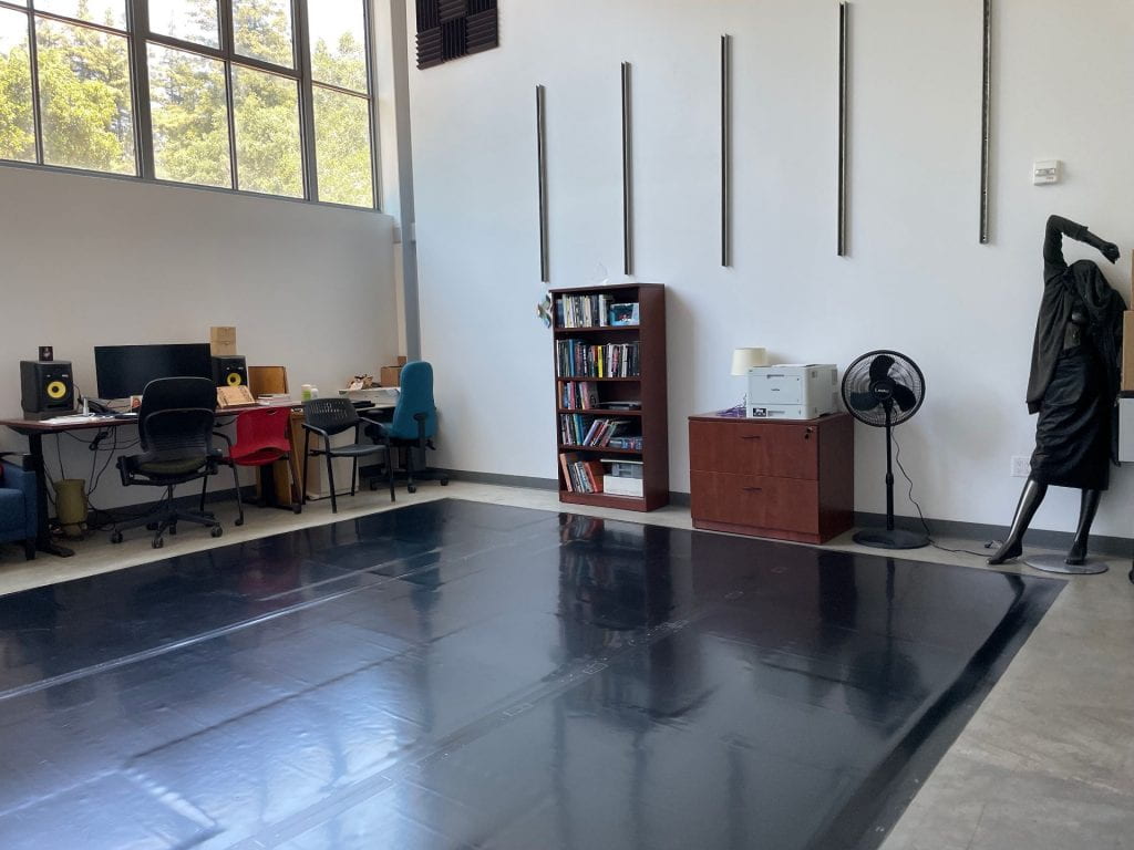 Image of the critical realities studio, with black dance floor, books and a mannqeuin with its arm raised